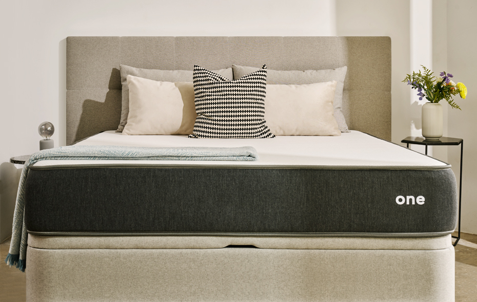 MaxColchón JustSleep One sobre un canapé tapizado beige, vista frontal con cabecero y cojines