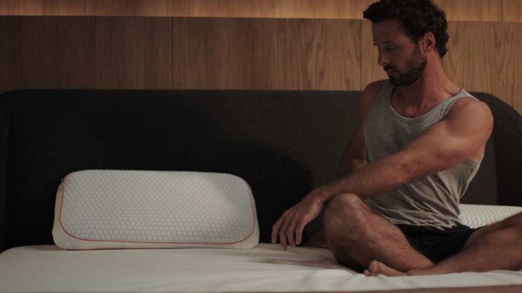 Hombre sentado en la cama junto a la almohada Emma Performance Adapt