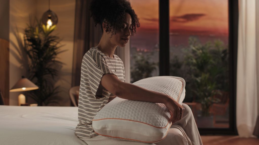 Mujer sentada en la cama abrazando la almohada Emma Performance Hybrid