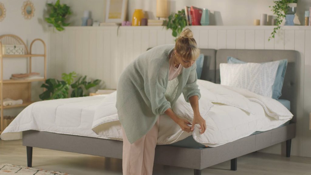 Mujer extendiendo el Edredón Emma 4 Estaciones sobre una cama tapizada